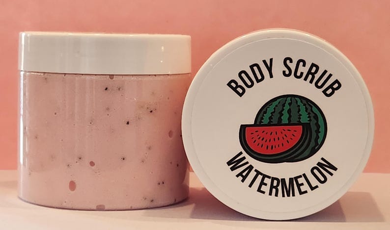 Op de afbeelding: Een witte pot met een roze lichaamsscrub erin. De pot heeft een wit deksel met de tekst "BODY SCRUB WATERMELON" erop gedrukt. Een watermeloen-schijf-afbeelding is ook op het deksel gedrukt.