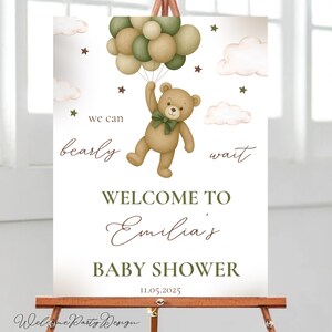 Puede incluir: Un letrero de baby shower con un oso de peluche sosteniendo globos. El letrero dice "Bienvenida a la Baby Shower de Emilia" con la fecha 11.05.2025. El diseño incluye nubes, estrellas y la frase "we can bearly wait."
