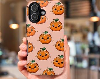 May include: A phone case featuring a repeating pattern of cartoon pumpkins with smiling faces, green leaves, and tan ribbons on a light pink background. The case has a black camera lens cutout.