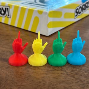 May include: Four game pieces for the board game Sorry! The pieces are shaped like hands giving the middle finger. The pieces are red, yellow, green, and blue.