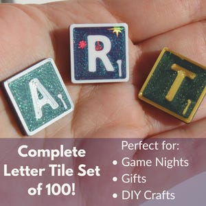 May include: Three Scrabble tiles spelling "ART" are displayed. The tiles have a glittery finish with white letters on teal and green backgrounds. The image also includes text that reads "Complete Letter Tile Set of 100!"