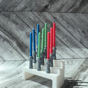 May include: A white plastic stand with nine lightsaber-shaped objects. The lightsabers are red, green, and blue. The stand is on a wood surface.