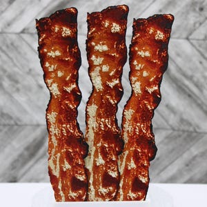 May include: Three strips of cooked bacon, arranged vertically, with a crispy texture and a rich brown color.