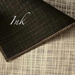 May include: A piece of fabric with a visible cross-hatch texture, featuring a dark charcoal black section folded over a lighter beige section. The word Ink is printed in white script on the dark fabric. The edges are finished with a stitched hem.