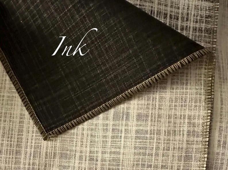 May include: A piece of fabric with a visible cross-hatch texture, featuring a dark charcoal black section folded over a lighter beige section. The word Ink is printed in white script on the dark fabric. The edges are finished with a stitched hem.