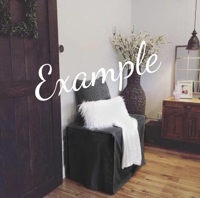 May include: A gray upholstered chair with a white throw blanket and a gray knitted pillow. The chair is in front of a white wall and a dark wooden door. A vase with white flowers is on the right side of the chair.