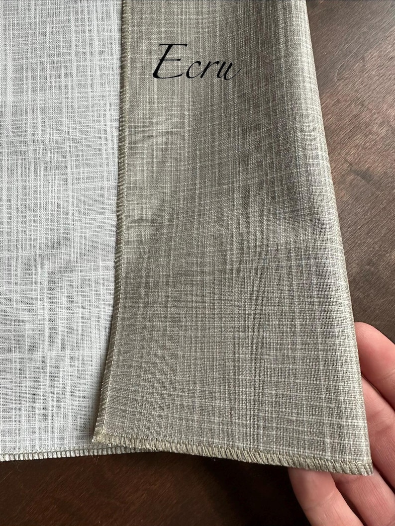 May include: A piece of fabric with a woven texture featuring a light grey side and a tan side labelled with the text Ecru. The material has a visible crosshatch pattern throughout, with a finished stitched edge separating the two distinct colour sections.