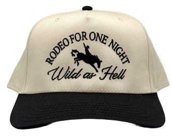 May include: A beige and black baseball cap with the text "Rodeo for One Night Wild as Hell" embroidered on the front. A silhouette of a cowboy riding a horse is also embroidered on the cap.