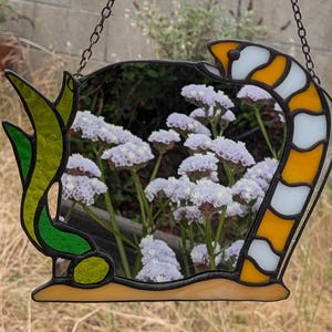 Könnte beinhalten: Buntglas-Fensterkunst in Schlangenform, mit Blick auf lila Blumen. Das Schlangendesign verwendet gelbes, weißes, grünes und schwarzes Glas und hat eine Kette zum Aufhängen. Ein einzigartiges Wohnaccessoire.