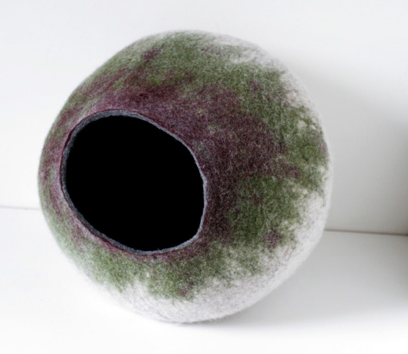 May include: A round, felted pet bed with a large opening. The bed is a mix of white, green, and purple.