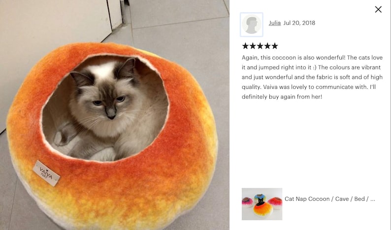 May include: A cat naps inside a bright orange and yellow felt cat bed. The bed is shaped like a cocoon and has a round opening. The bed is labeled "Vaiva Cat".