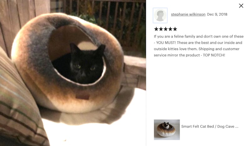 May include: A black cat resting inside a brown and white felt cat bed. The bed is shaped like a cave and has a soft, plush interior. The cat is looking out of the bed with its eyes open.