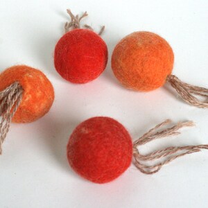 May include: Four felt balls with brown string tails. The balls are orange and red.
