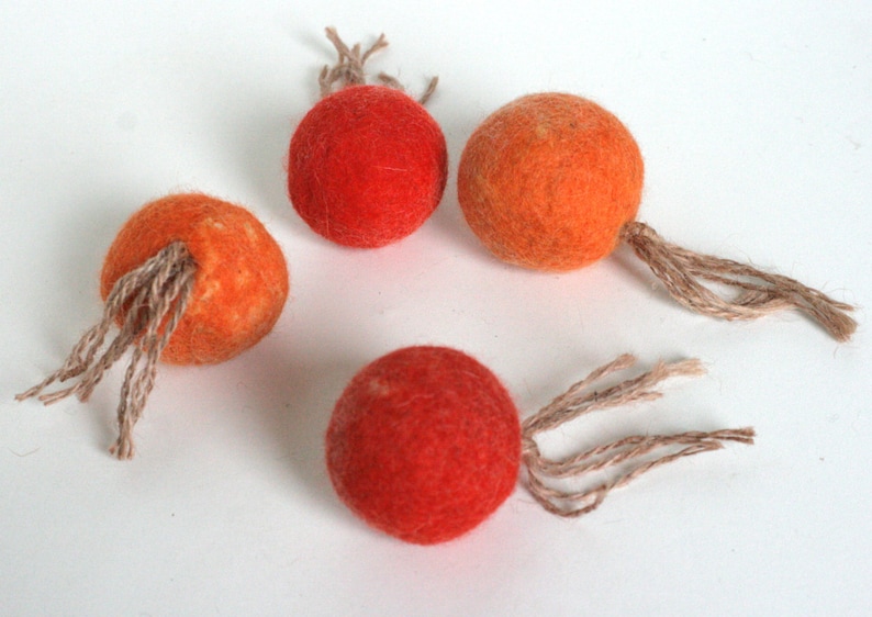 May include: Four felt balls with brown string tails. The balls are orange and red.