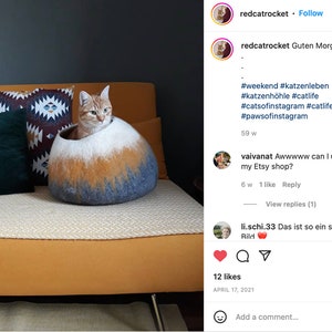 May include: A ginger cat sits inside a gray, white, and orange felted cat bed. The bed is on a yellow couch with a black and white patterned pillow and a dark green pillow. The cat is looking at the camera. The image is from an Instagram post with the caption "Guten Morgen" and hashtags related to cats and cat beds.