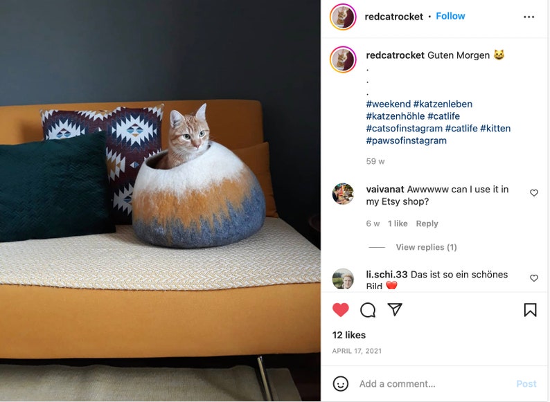 May include: A ginger cat sits inside a gray, white, and orange felted cat bed. The bed is on a yellow couch with a black and white patterned pillow and a dark green pillow. The cat is looking at the camera. The image is from an Instagram post with the caption "Guten Morgen" and hashtags related to cats and cat beds.
