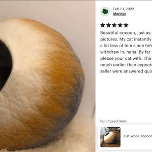 May include: A white, yellow, and gray cat bed shaped like a sphere with a cat inside. The bed is made of wool felt and has a round opening for the cat to enter.