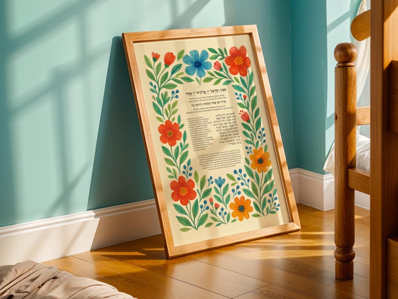 May include: A framed print with a floral border featuring red, blue, and orange flowers. The print has text in Hebrew. The frame is made of light-colored wood, and the background is a light beige color.