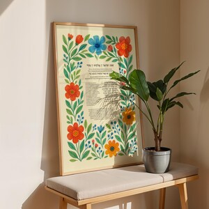 Peut inclure: Une affiche encadr&eacute;e avec du texte en h&eacute;breu, entour&eacute;e d'une bordure florale de fleurs rouges, bleues et jaunes avec des feuilles vertes. L'affiche est sur un banc clair avec une plante en pot.