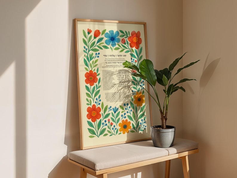 Peut inclure: Une affiche encadr&eacute;e avec du texte en h&eacute;breu, entour&eacute;e d'une bordure florale de fleurs rouges, bleues et jaunes avec des feuilles vertes. L'affiche est sur un banc clair avec une plante en pot.
