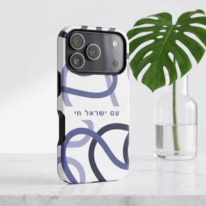 Puede incluir: Una funda de smartphone blanca con un patrón de líneas curvas superpuestas en azul oscuro y claro. El texto hebreo "עם ישראל חי" está impreso en azul en el centro. La funda tiene un área de cámara negra con tres lentes circulares.