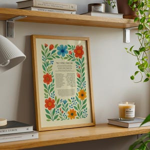 Peut inclure: Une affiche encadr&eacute;e avec une bordure florale dans un cadre en bois. L'affiche pr&eacute;sente du texte en h&eacute;breu et des fleurs color&eacute;es en rouge, bleu et jaune. L'affiche est expos&eacute;e sur une &eacute;tag&egrave;re en bois avec une lampe et des livres.