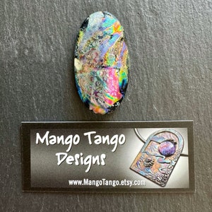 May include: A colorful, iridescent glass oval pendant with a black background. The pendant has a variety of colors, including pink, purple, blue, and green. The pendant is approximately 1 inch in length. The pendant is made by Mango Tango Designs.