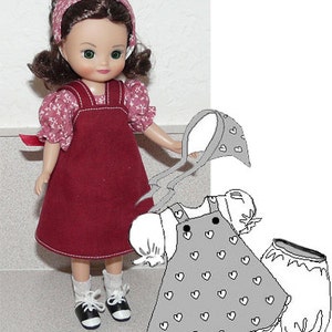 May include: A doll wearing a burgundy jumper dress with white floral sleeves and a matching headband. The doll is also wearing white socks and black and white shoes. A drawing of a similar outfit with heart patterns is next to the doll.