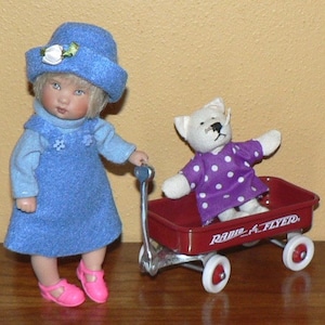 May include: A doll wearing a blue dress and hat is pushing a red Radio Flyer wagon with a white teddy bear wearing a purple polka dot dress inside.
