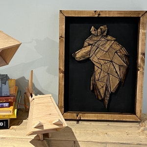 Peut inclure: Une sculpture de tête de loup en bois dans un cadre brun avec un fond noir. La sculpture est faite de nombreuses petites pièces de bois disposées en un motif géométrique. La tête du loup est tournée vers la droite. La sculpture est sur une table en bois avec une lampe en bois et une pile de livres.