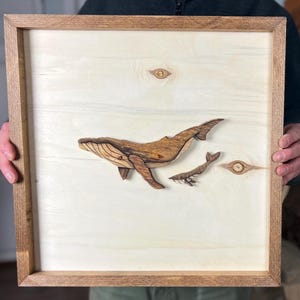 Peut inclure: Une œuvre d'art murale en bois représentant une baleine à bosse sculptée et une baleine plus petite, toutes deux dans des tons de brun, sur un fond de bois clair.