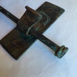 May include: A rustic, green-colored metal towel bar with a decorative knob on the end. The bar is mounted to a rectangular metal plate.