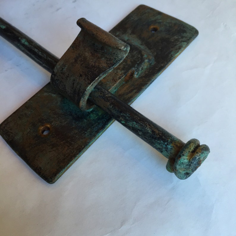 May include: A rustic, green-colored metal towel bar with a decorative knob on the end. The bar is mounted to a rectangular metal plate.