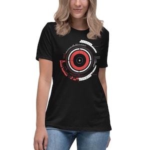 May include: Black t-shirt featuring a red and white circular graphic design. The circle has a smaller black circle in the centre and text around the outer edge.