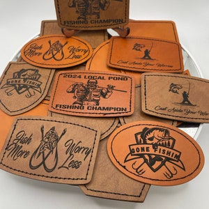 May include: A collection of brown leather patches with various fishing-themed designs. The patches feature text such as "Gone Fishin", "Fish More Worry Less", and "Cast Aside Your Worries". Some patches also feature images of fish, fishing rods, and a person fishing.