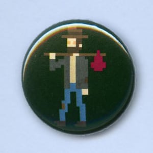 May include: A green button with a pixelated image of a person wearing a hat and carrying a red bag. The person is wearing a gray jacket and blue jeans.