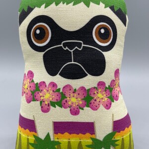 May include: A plush toy pug wearing a green lei and pink flower necklace. The pug has brown eyes and a black nose and mouth. The toy is standing on a green and yellow patterned surface.