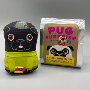 May include: A black pug soft toy wearing a green sweater and a hat. The toy is approximately 10 cm tall. Beside it is a package labelled "PUG SURPRISE Series 13" with a pug illustration.