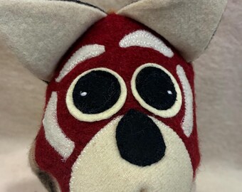 May include: A handcrafted felt plush head of a red fox with large pointed ears, oversized black circular eyes, white eyebrows, and a black nose. The face features a deep red base colour with cream-coloured accents on the ears, muzzle, and forehead.