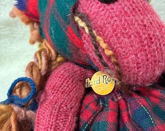 May include: A handmade pink horse doll with a Hard Rock Cafe tag. The horse has large black button eyes, a plaid patterned mane, and a red and green plaid dress. The doll's mane and tail are made of yarn.
