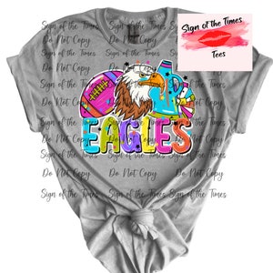 May include: A gray t-shirt with a colorful graphic design featuring an eagle, football, and the word "EAGLES". The design is surrounded by the text "Sign of the Times Do Not Copy" repeated multiple times.
