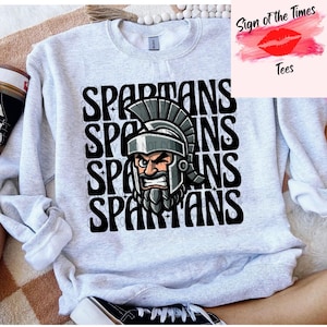 May include: A gray sweatshirt with a graphic design of a Spartan warrior's head with a helmet and beard. The word "SPARTANS" is repeated four times in black text.