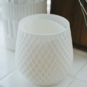 May include: White ceramic planter with a diamond pattern. The planter is empty and sitting on a white tiled surface.