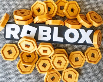 May include: A collection of gold-colored, hexagonal tokens with a square center, scattered around a black and white "ROBLOX" logo. The tokens are likely game currency or collectibles, set against a textured gray background.