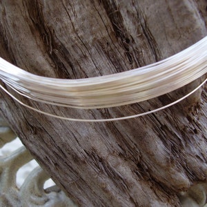 May include: A close-up of a spool of silver wire, wound tightly and resting on a piece of weathered wood.