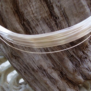 May include: A close-up of a spool of silver wire, the wire is wound tightly and is a light silver color. The wire is sitting on a piece of weathered wood.