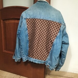 Op de afbeelding: Een blauwe denimjas met een bruin en wit gepatroneerd stoffen paneel op de rug. De jas heeft een sherpa voering.