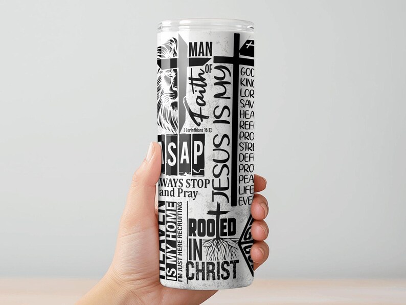May include: A white tumbler with black text and graphics. The design includes the words "Faith," "Jesus is My," and "Rooted in Christ," along with a lion illustration and a cross. The tumbler is held by a hand.