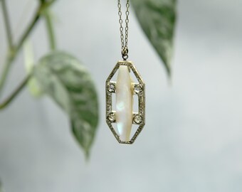 May include: A silver pendant necklace with a white oval-shaped gemstone set in a geometric frame. The frame is decorated with small clear gemstones.