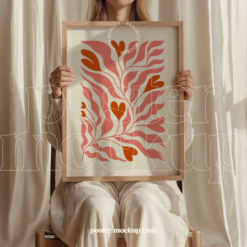 May include: A woman holds a framed poster with a pink and white abstract design featuring stylized leaves and hearts. The poster is in a wooden frame and has the text "QUALITY - REALISTIC MOCKUP - HIGH" printed on the top.
